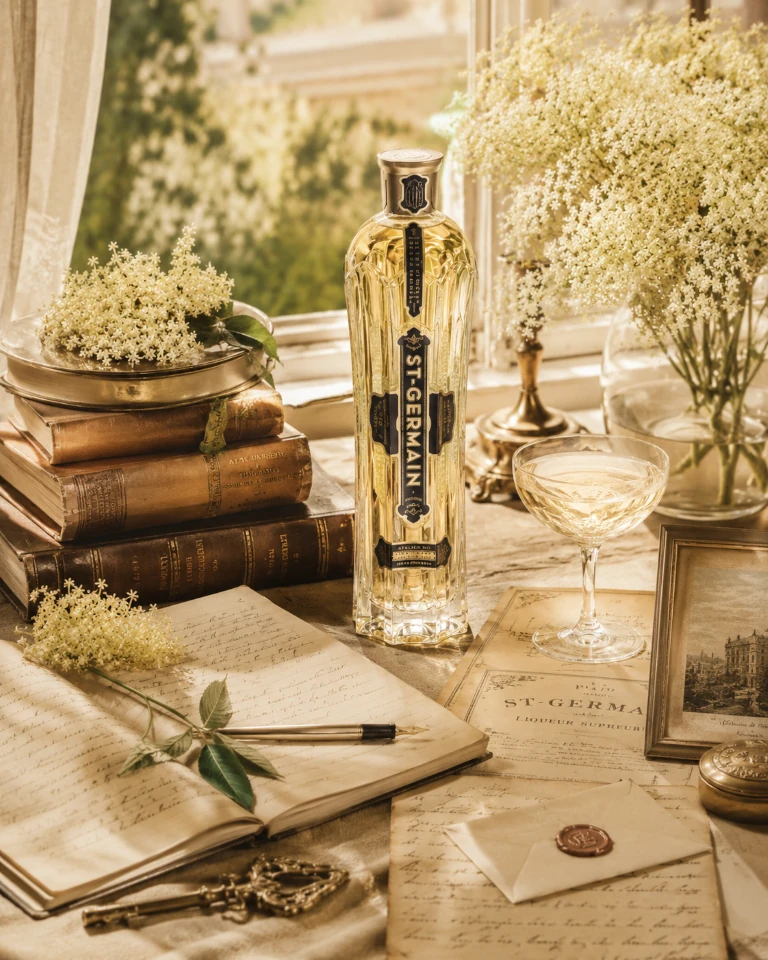 St-Germain Flasche mit alten Büchern, handgeschriebenem Journal und Holunderblüten